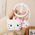 A hand holding a white coiled charging cable with two Hello Kitty-shaped USB-C adapters, one with a pink bow and one with a black bow, against a soft beige indoor background.
