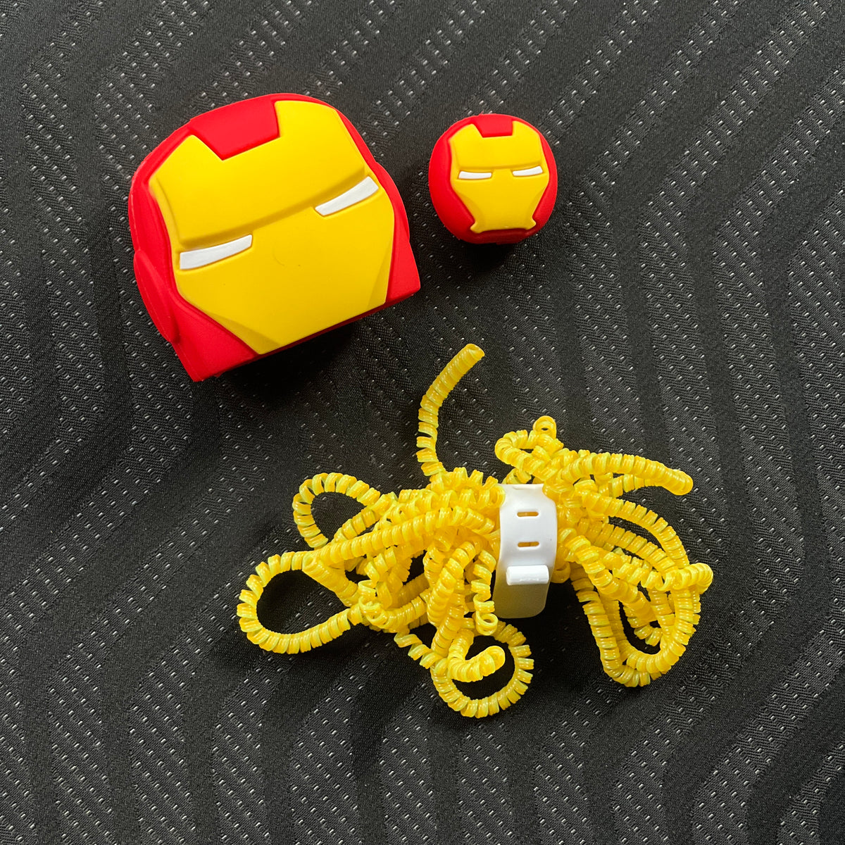 Two Iron Man helmet-shaped earbud cases and a yellow toy motorcycle on a textured black surface.